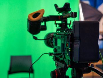Professional video camera on a stand with green chromakey in a studio